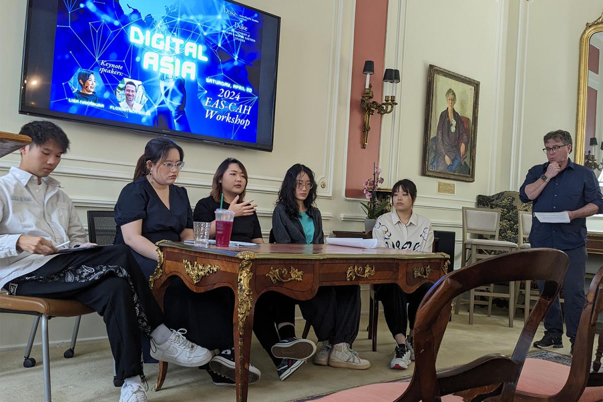Five graduate student panelists sit at at table while the faculty moderator faces them at the far right
