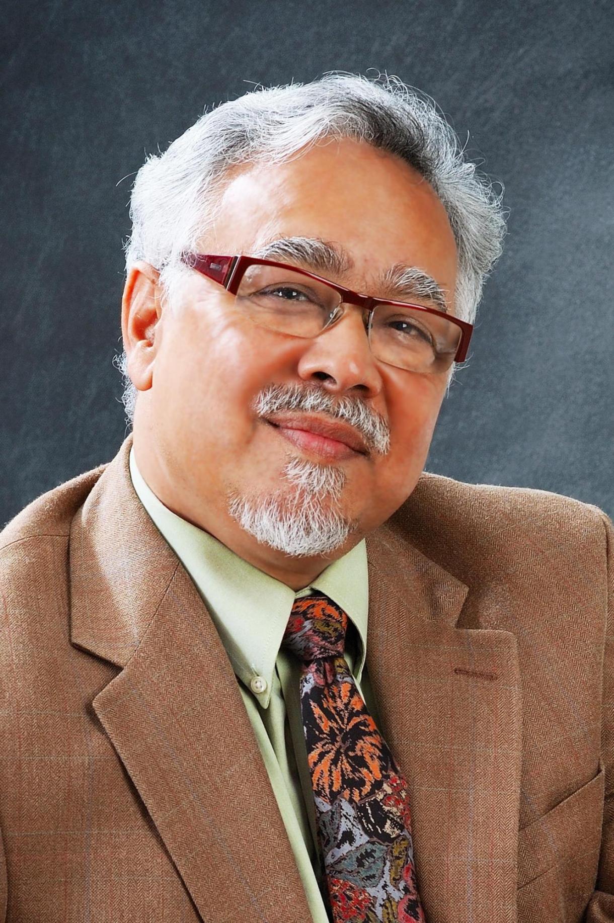 Prasenjit Duara; a person wearing a brown suit with a green shirt, a patterned tie, and glasses