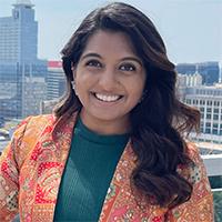 A person wearing a green shirt and orange paisley jacket in front of an urban skyline