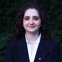 A person wearing a white shirt and dark suit jacket with a small lapel pin