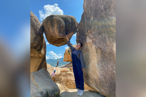 A person standing next to a boulder balanced between two larger rocks