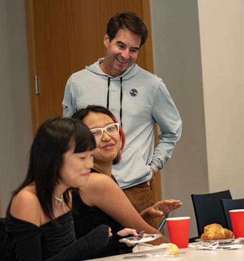 A man (standing) speaks with two women (seated)