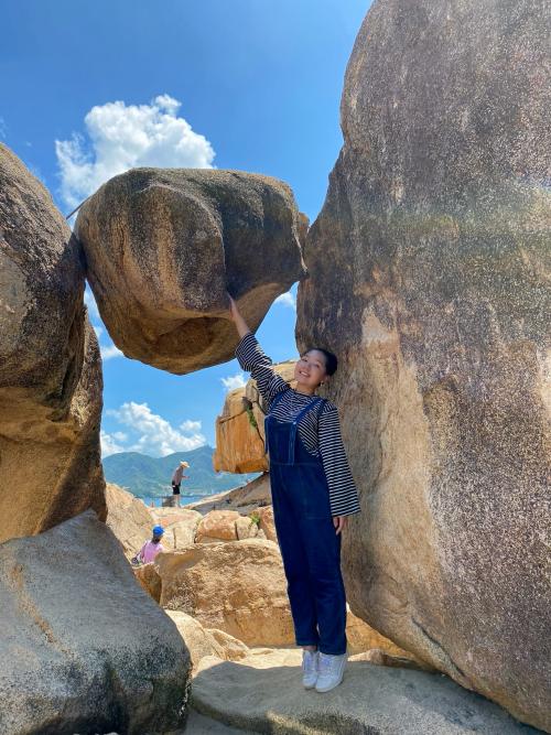 A person standing next to a boulder balanced between two larger rocks