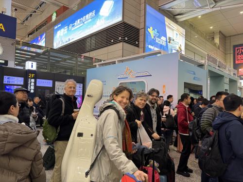 A small group of people carrying instrument cases and luggage walk through a busy train station in Shanghai