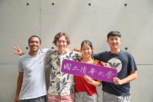 Group of students smiling at the camera holding a sign in Chinese (translation: "National Tsing Hua University")